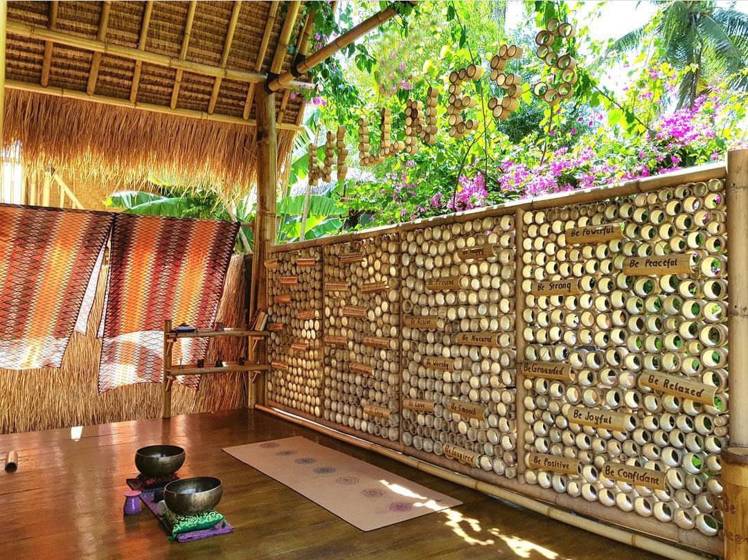 A room with a bamboo wall displaying motivational phrases, a thatched roof, and a view of lush greenery.