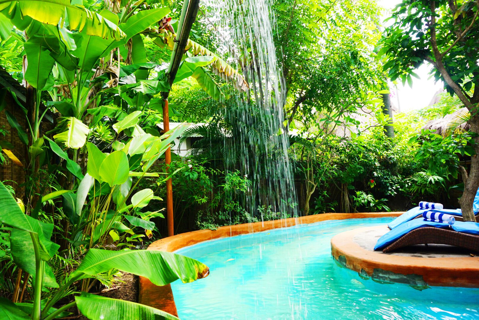 Una piscina con cascada rodeada de abundante vegetación.