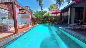 A swimming pool with lounge chairs and a thatched-roof structure.