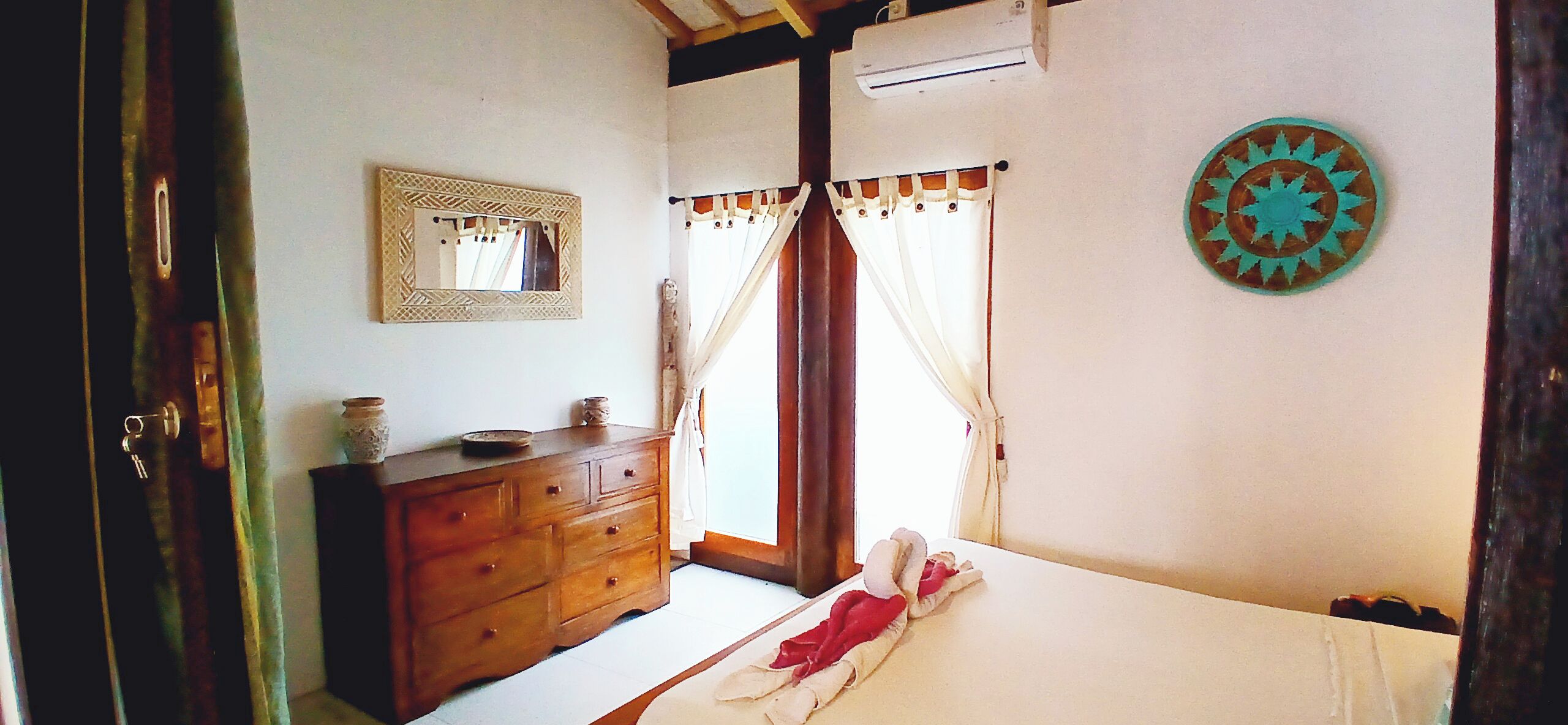 Un dormitorio con un aparador de madera, una cama con edredón blanco, un espejo y un plato decorativo en la pared.