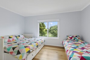 A bedroom with two beds, a window with a view of greenery, and a white ceiling. - Len's Place (Lorne)