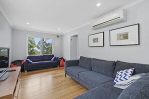 A modern living room with a grey sofa, a television, and a wooden floor.