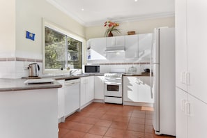 A modern kitchen with white cabinetry, a stove, microwave, and a refrigerator.