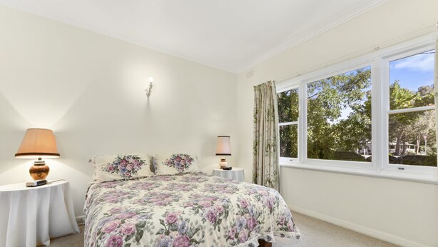 A bedroom with a floral bedspread, two bedside lamps, a nightstand, and a window with curtains.