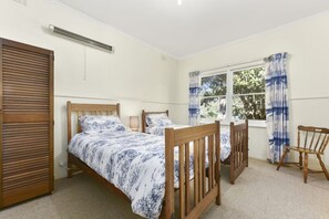 A bedroom with two single beds, a window with curtains, a radiator, and a wooden chair. - Charles (Lorne)