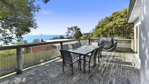 A wooden deck with a table and chairs, a barbecue grill, and a view of the sea.