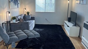 Een moderne woonkamer met een bank, fauteuils, een zwart vloerkleed, een televisie en kunst aan de muren.