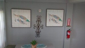 Una habitación con dos obras de arte enmarcadas, una pieza decorativa de metal, un extintor y una planta pequeña sobre una mesa.