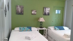Una habitación con dos camas, una mesita de noche con lámpara y una puerta verde.