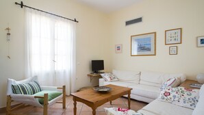 Un salon avec un canapé, une table en bois, une chaise, un téléviseur et une fenêtre avec des rideaux.