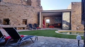 Een gebouw van natuursteen met een moderne glazen uitbouw, terras en een zwembad.