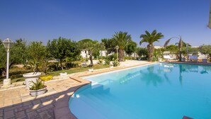Una piscina de borde curvo, rodeada de macetas y palmeras.
