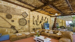 Una habitación rústica con pared de piedra, vigas de madera, un sofá con cojines estampados y una mesa de centro blanca.