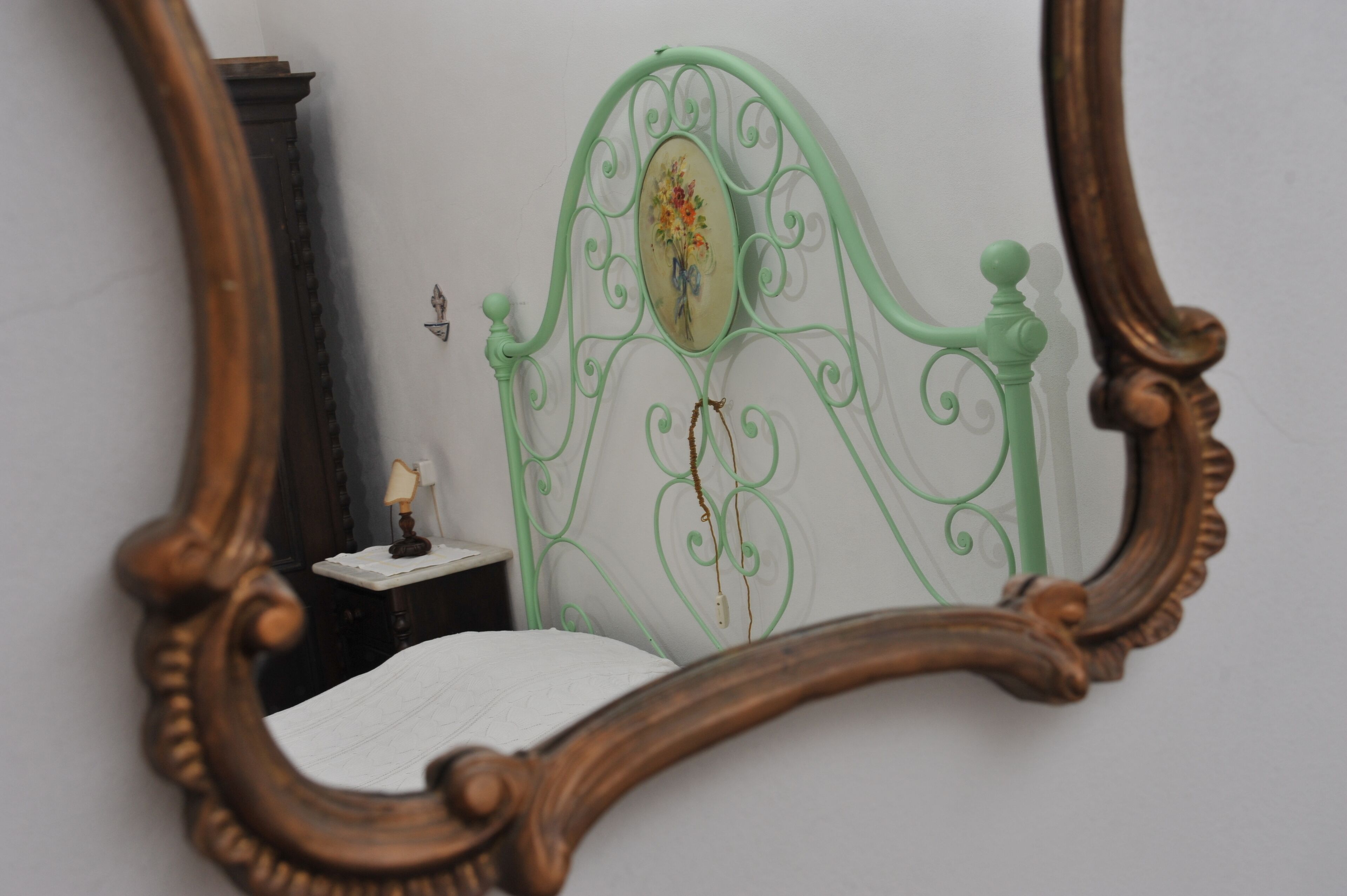 Una camera da letto con una testiera in metallo verde, un comodino con una lampada e uno specchio con cornice decorata.
