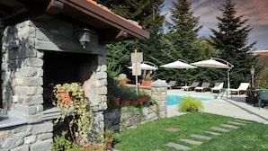 A stone building with a fireplace, surrounded by potted plants and a pool area with lounge chairs and umbrellas. - VILLA BENEDETTA, Casa Marcello # 2 (Sillicano in Garfagnana, Italia)