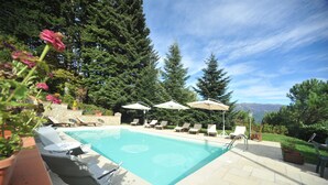 A pool area with lounge chairs and umbrellas, surrounded by trees and a view of mountains. - VILLA BENEDETTA, Casa Marcello # 2 (Sillicano in Garfagnana, Italia)