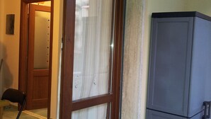 A room with a sliding glass door leading to a hallway, a small table with a chair, and a grey refrigerator. - New apartment 250 m from the beach (Alghero)