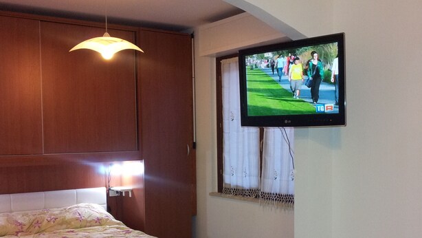 A bedroom with a bed, a television mounted on the wall, and a window with curtains. - New apartment 250 m from the beach (Alghero)