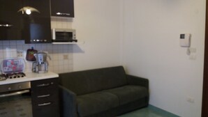 A compact kitchen with dark cabinets, a microwave, a toaster, and a small refrigerator. - New apartment 250 m from the beach (Alghero)
