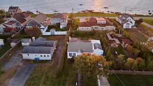 Vista aérea de una zona residencial con casas, cielo despejado y un atardecer sobre el agua.