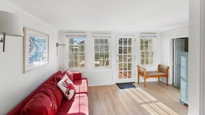 Una habitación luminosa con un sofá rojo, un banco de madera y un aparador de vidrio.