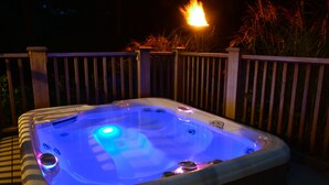 A hot tub with blue lighting, surrounded by a wooden deck and a fire in the background.