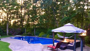 A backyard with a swimming pool, a covered seating area, and a fire pit.
