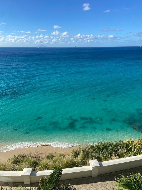A beach with clear turquoise water and a distant sailboat.