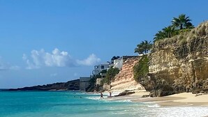 A beach with clear turquoise water, a sandy shore, and a rocky cliff with buildings on top. - The Cliffs 2BR 2.5BA Apt Private Beach Sleeps 5
Luxury Oceanfront Apartment (Cupecoy)