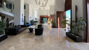 A spacious lobby with a high ceiling, a seating area with sofas and a coffee table, and potted plants. - The Cliffs 2BR 2.5BA Apt Private Beach Sleeps 5
Luxury Oceanfront Apartment (Cupecoy)