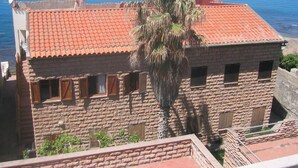 A stone building with a red-tiled roof, a palm tree in front, and a view of the sea. - Villa Bosa, Waterfront apartment in Bosa area, 10 meters from beach WI (trasnuraghes)