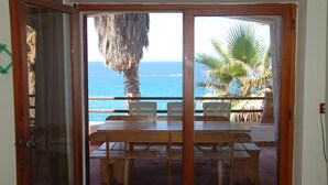 A room with a wooden table and chairs, a large window with a view of the ocean and palm trees. - Villa Bosa, Waterfront apartment in Bosa area, 10 meters from beach WI (trasnuraghes)