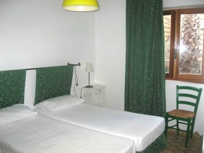Une chambre avec deux lits simples, une petite table de chevet avec une lampe, une chaise et une fenêtre avec des rideaux.