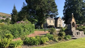 A landscaped garden with a stone monument, a stone building, and a well-maintained lawn.