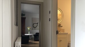 A hallway leading to a living area with a round mirror, a radiator, and a small table with flowers.