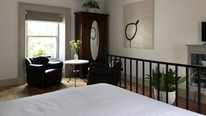 A bedroom with a bed, a desk with a chair, a potted plant, a television, and a window with natural light.