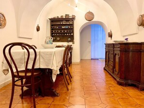 A dining area with a long table, chairs, a cabinet with dishes, and a door leading to another room.
