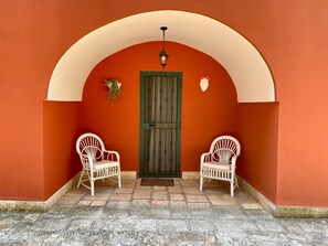 An arched doorway with a green door, two white wicker chairs, and a hanging plant.