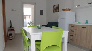 A compact kitchen with a white table and green chairs, a refrigerator, and wooden cabinets. - Saturday-Saturday-L'ondazzurra stays: a vacation without contingencies!  (Marina di Mancaversa)