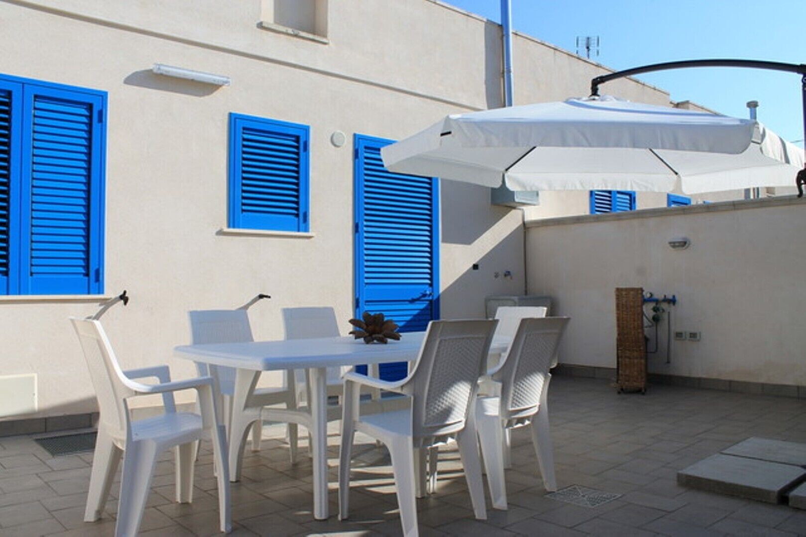 An outdoor patio with a table and chairs, a white umbrella, and blue shutters on the building.
