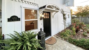 A white house with a black door, a window, and a porch with a doormat.