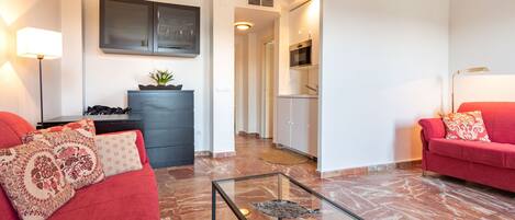 A modern living room with a red sofa, a glass coffee table, and a kitchen in the background.