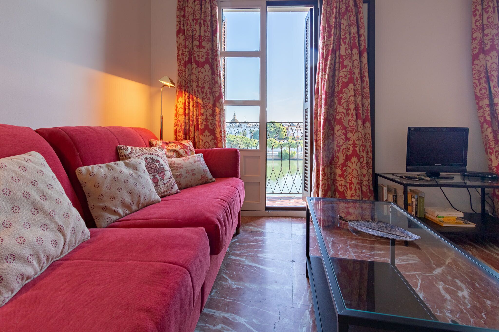 A living room with a red sofa, patterned cushions, a glass coffee table, and a television.