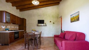 A kitchen with wooden cabinets, a dining table with chairs, a red sofa, and a painting of sunflowers on the wall.