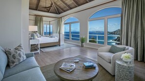 Un'ampia stanza con un letto grande, un'area salotto con tavolino e vista sul mare attraverso ampie finestre.