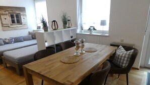 Un coin repas avec une table en bois, quatre chaises et un canapé à l’arrière-plan.
