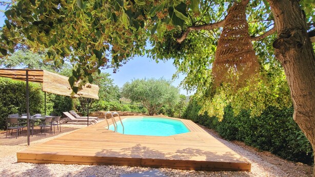 A wooden deck with a pool, surrounded by greenery and a pergola with seating. - Quality charming house classified 3* with private pool and air conditionning (La Caunette)