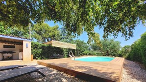 A swimming pool with a wooden deck, surrounded by pebbles and trees. - Quality charming house classified 3* with private pool and air conditionning (La Caunette)