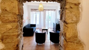 A living room with a stone archway, a sofa, two armchairs, a TV, and a chandelier. - Quality charming house classified 3* with private pool and air conditionning (La Caunette)