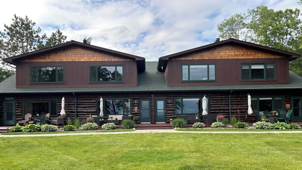 A log cabin with two main levels, large windows, and a well-maintained lawn.